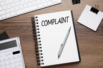 Notebook with word Complaint, computer keyboard, calculator and stationery on wooden table, flat lay