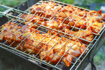 Spicy marinated chicken wings and legs on grill and on a summer barbecue. Cooking process on flame in braizer outside. BBQ, picnic, street food.