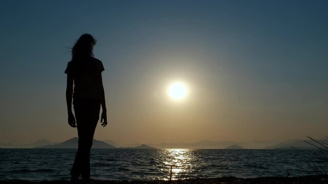 Silhouette of girl show thumb up. A happy teen silhouette walk along the beach and show the thumb up tp the sea during sunset in summer.