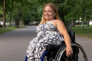 Smiling Happy Young Woman With Short Stature On Wheelchair Enjoys Time in Green Park At Summer Day. Female Adult With Disability. Copy Space For Text. Horizontal Plane