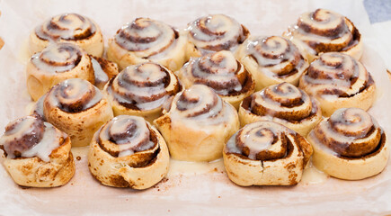 Soft and fluffy cinnamon swirls topped with sugar glaze on wooden background..