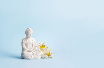 Buddha figurine and flowers on blue background. Mental health and meditation concept. Soft focus, copy space.