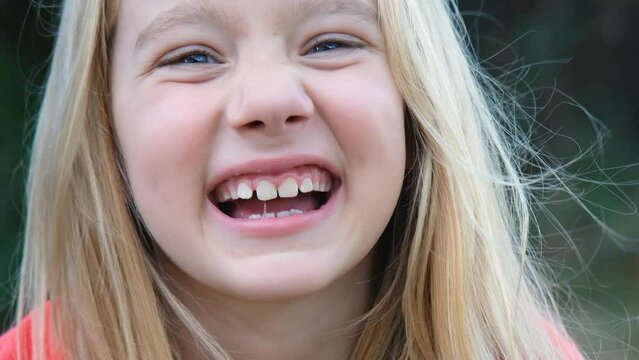 Video portrait of a blond child looking at the camera and laughing. Happy child of seven years smiling.