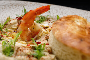 Hummus with shrimp, peanuts, chickpeas and a bun, on a plate. close up