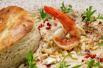 Hummus with shrimp, peanuts, chickpeas and a bun, on a plate. close up