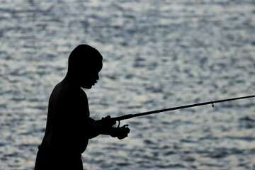 Campos dos Goytacazes, RJ, Brazil, 08/19/2023 - Boy in silhouette fishing at the sunset in Paraiba do Sul river