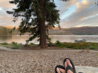 Relaxing feet with flip-flops on the edge of lake at golden sunset
