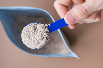 Male hand takes out a protein powder from a bag on a brown background close-up top view.