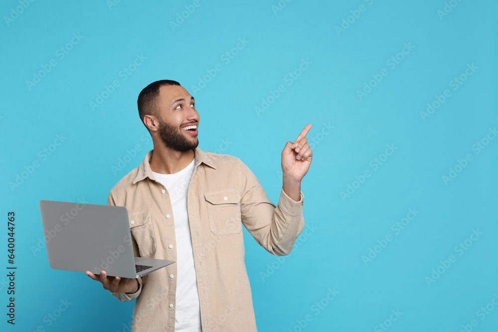 Poster smiling young man with laptop on light blue background, space for text