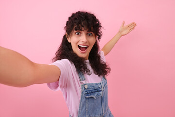 Beautiful woman taking selfie on pink background