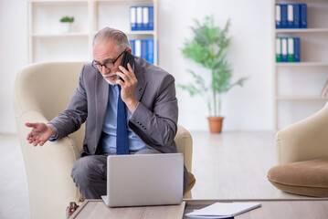 Old male employee speaking by phone at workplace