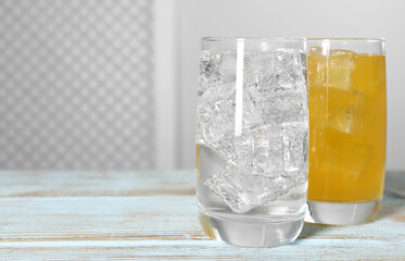 Glasses of different refreshing soda water with ice cubes on light blue wooden table, space for text