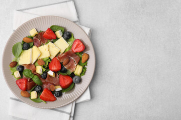 Tasty salad with brie cheese, prosciutto, almonds and berries on light grey table, top view. Space for text