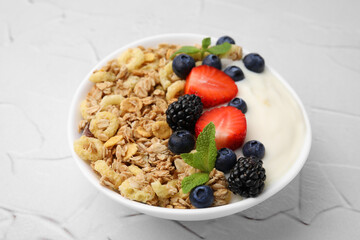 Tasty oatmeal, yogurt and fresh berries in bowl on white textured table, closeup. Healthy breakfast