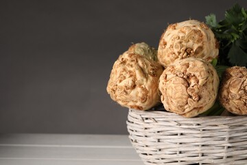 Fresh raw celery roots in wicker basket on white wooden table, closeup. Space for text