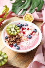 Tasty smoothie bowl with fresh kiwi fruit, berries and granola on pink table