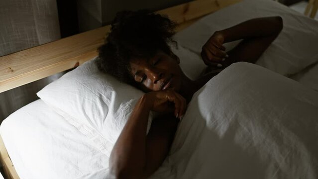 African american woman lying on bed waking up stretching arms at bedroom