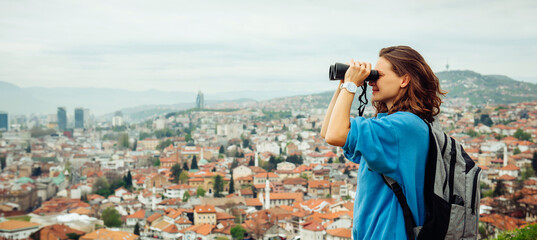 A beautiful girl traveler looks through binoculars at Sarajevo, the capital of Bosnia and...