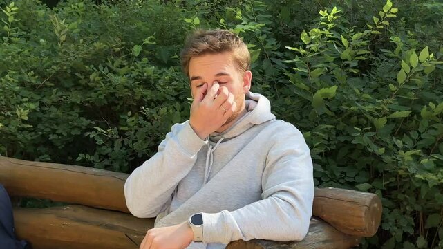 handsome young man resting on a park bench and squint at the sun