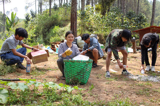 Group of friends picking up waste garbage plastic bottles from the forest, cleaning up nature. Ecology and earth day concept