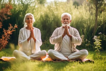 A retired Caucasian couple in eco-friendly clothing meditate in the yoga lotus position in a garden.