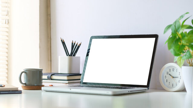 Mock up laptop computer, coffee cup and potted plant on white table. Empty screen for your advertise text.