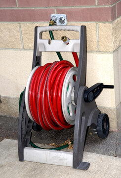An outdoor garden hose wound on a reel storage unit, with handle showing. The unit is on wheels for portability.