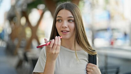 Young beautiful girl student wearing backpack sending voice message by smartphone at street