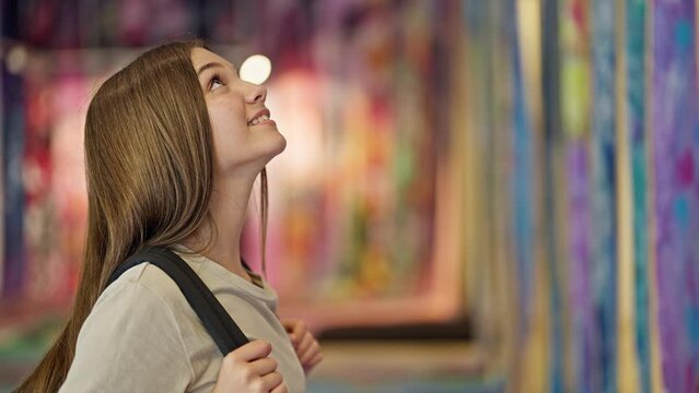 Young beautiful girl student wearing backpack looking around smiling at art gallery
