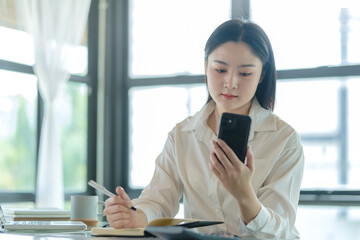 Obraz premium Asian female employees checking social media, reading online news on her smart phone.