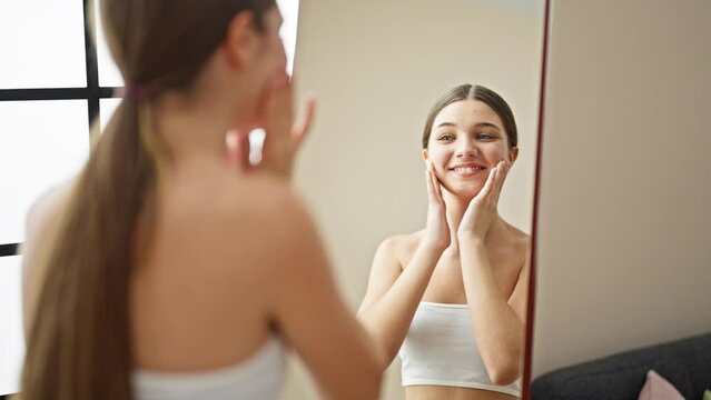 Young beautiful girl massaging face looking on mirror at home