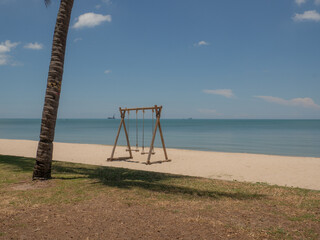 wooden swing tied with rope by the beach. beautiful tropical nature landscape. overlooking the bright green sea far and wide. the sky is bright and clear.