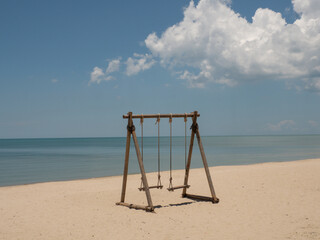 wooden swing tied with rope by the beach. beautiful tropical nature landscape. overlooking the bright green sea far and wide. the sky is bright and clear.