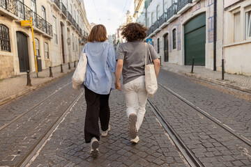 Fototapeta premium Back view of couple in love holding hands while walking on old city street. High quality photo