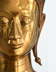 Close-up face of golden Buddha statue, white scene