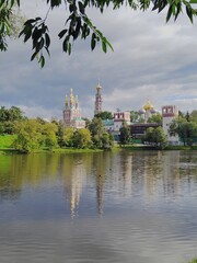 Picturesque view of Novodevichy Monastery on cloudy summer day. Oldest stronghold of Orthodoxy. Mother of God-Smolensk Novodevichy Convent in Moscow. Reflection of buildings on water surface of pond