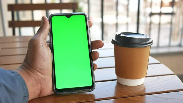 Holding Smart Phone With Green Screen And Take Away Paper Coffee Cup On Table 