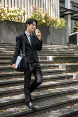 A businessman is sipping coffee while walking down the stairs in front of the building.