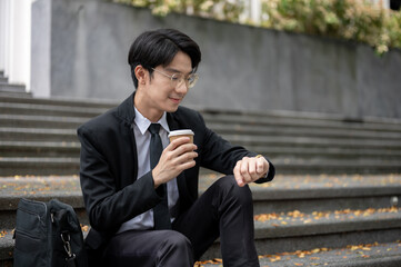 A businessman is sipping coffee and checking time on his watch while sitting on a staircase