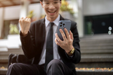 Fototapeta premium Cropped image, A cheerful Asian businessman receiving good news on the phone, got a new job