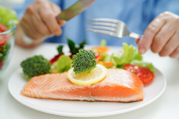 Asian elderly woman patient eating salmon stake and vegetable salad for healthy food in hospital.