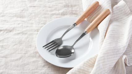 White plate with fork and spoon and napkin on linen table cloth background