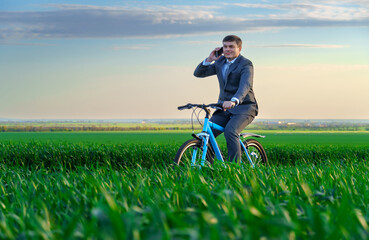 a businessman rides a bicycle through a green grass field, makes a phone call, the concept of activity, recreation or freelancing