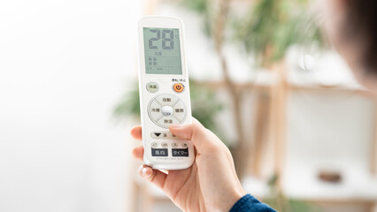 リモコンでエアコンの温度を確認する女性