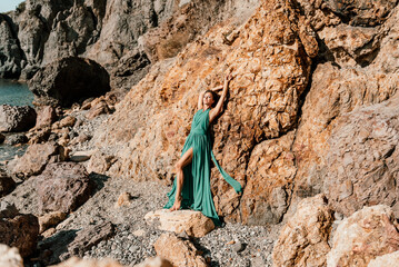 Woman green dress sea. Woman in a long mint dress posing on a beach with rocks on sunny day. Girl on the nature on blue sky background.