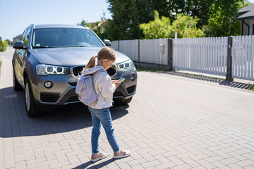 Child looks at a cell phone while crossing a road in front of the car. Concept of mobile phone addiction.