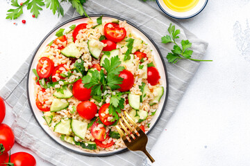Bulgur tabbouleh salad with tomatoes, cucumbers and parsley. Traditional Middle Eastern dish. White table background, top view