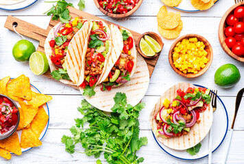 Taco party.  Served table with tortillas, nachos, sauces, appetizers and plates. Homemade mexican food cooking scene. White table background, top view
