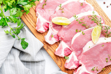 Raw pork chops, loin  on wooden cutting board prepared for cooking with garlic, thyme, spices and...