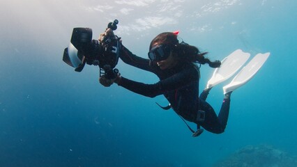 Female Indian underwater photographer swims with big underwater camera. Female freediver with camera swims in the sea